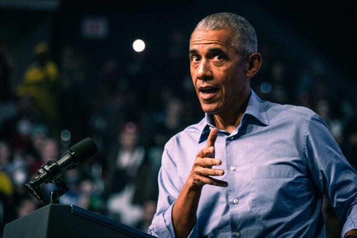 shutterstock_2231134745.jpg featured image Barack Obama in blue shirt speaking at podium with microphone.