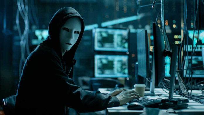 shutterstock_680078920.jpg featured image Person in hoodie and mask using computer, multiple screens.