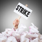 Hand holding strike sign amid crumpled paper pile