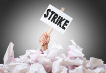 Hand holding strike sign amid crumpled paper pile