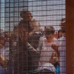 Group of people behind a wire fence.