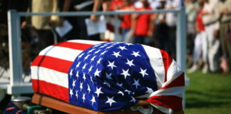 American flag draped over a casket at ceremony.