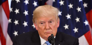 Donald Trump speaking with American flags in background.