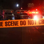 Crime scene tape with emergency vehicles in background.