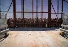 People standing behind a fence on a dusty path