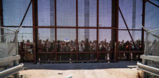 People standing behind a fence on a dusty path