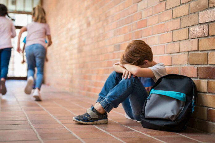 Sad child sitting against brick wall kids running away