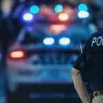 Police officer stands near patrol car with lights flashing