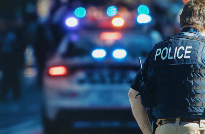 Police officer stands near patrol car with lights flashing