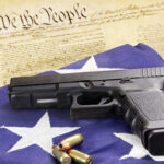 A handgun resting on an American flag with bullets and a historical document in the background