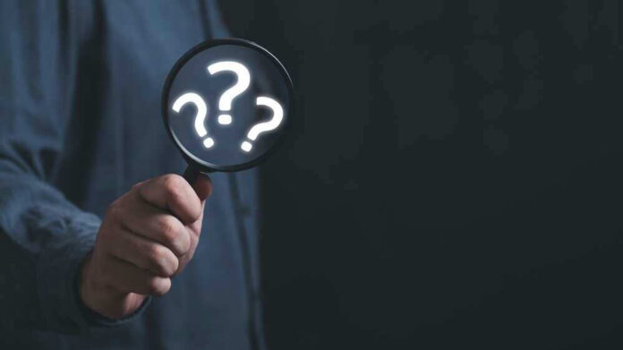 Hand holding magnifying glass with question marks.