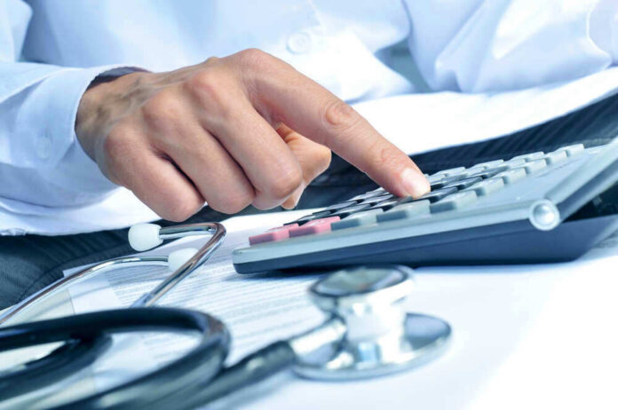 Doctor using calculator with stethoscope on the table.