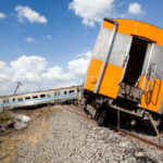 Derailed train car leaning off the tracks with another train in the background