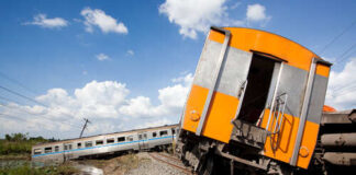 Derailed train car leaning off the tracks with another train in the background