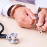 A handcuffed doctor holding a surgical scalpel next to a stethoscope