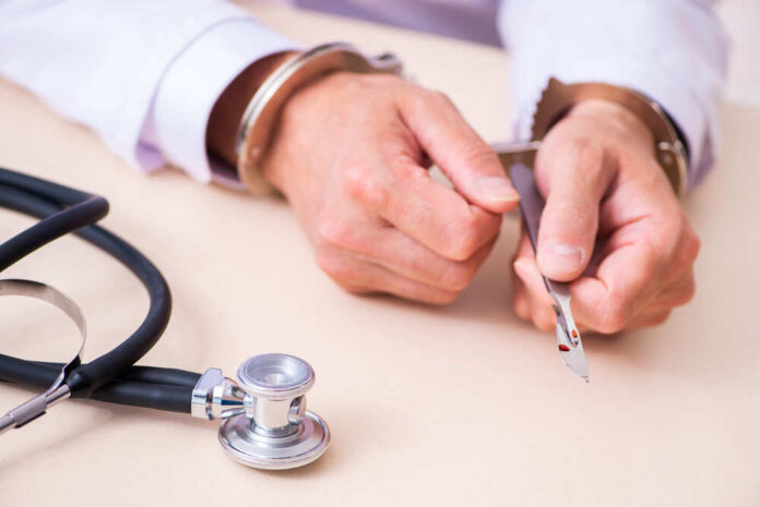 A handcuffed doctor holding a surgical scalpel next to a stethoscope