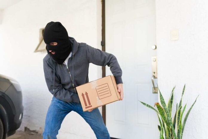 A masked individual stealing a package from a doorstep