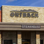 Exterior view of an Outback Steakhouse restaurant with a stone facade
