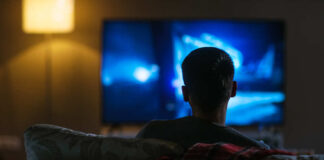 Person sitting on a couch watching a television screen in a dimly lit room