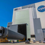 Massive rocket component outside NASA assembly building under clear sky.