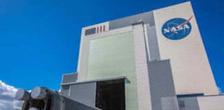 Massive rocket component outside NASA assembly building under clear sky.