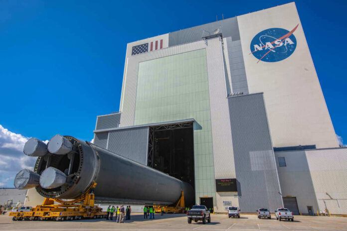 Massive rocket component outside NASA assembly building under clear sky.