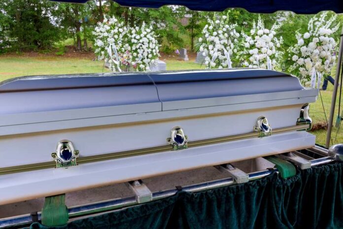 A casket at a graveside surrounded by floral arrangements