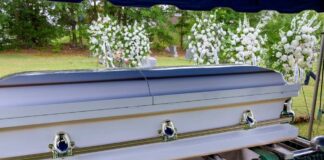 A casket at a graveside surrounded by floral arrangements