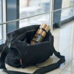 A black travel bag with rolled documents inside, placed on a tiled floor near a window
