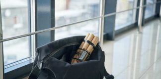 A black travel bag with rolled documents inside, placed on a tiled floor near a window