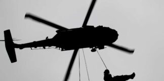 Silhouette of a helicopter with two individuals being lowered by ropes