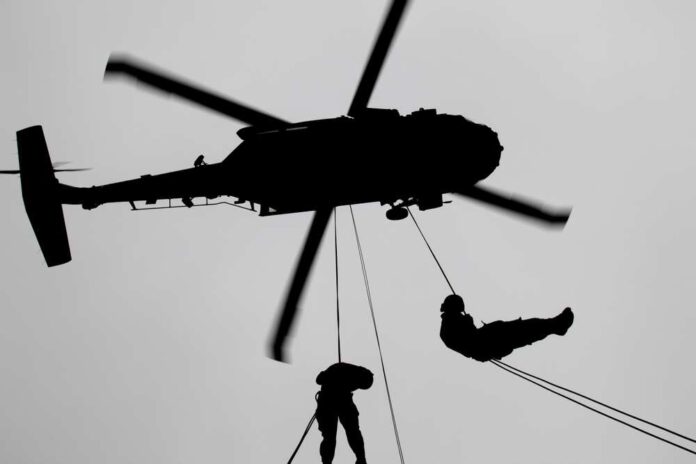 Silhouette of a helicopter with two individuals being lowered by ropes