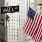 Street signs for Wall Street and Broad Street with American flags in the background