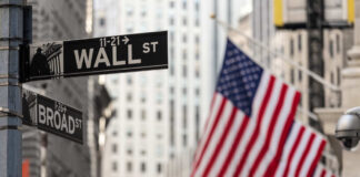 Street signs for Wall Street and Broad Street with American flags in the background