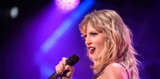 Taylor Swift performing with microphone on stage, colorful lighting.