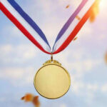 Olympic Medals SHATTER in Winners’ Hands Gold medal with blue, white, red ribbon, sky background.