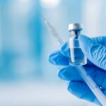 A gloved hand holding a syringe and a vial of liquid