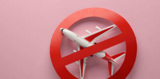 Airplane inside red prohibition sign on pink background.