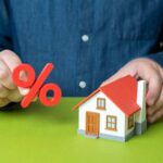 Biden Mortgages Trap Millions Person holding a percentage symbol above a model house