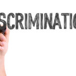 A hand holding a marker writing the word 'DISCRIMINATION'