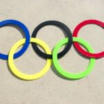 Olympic Star’s Neck BROKEN! Colorful Olympic rings arranged on sandy surface
