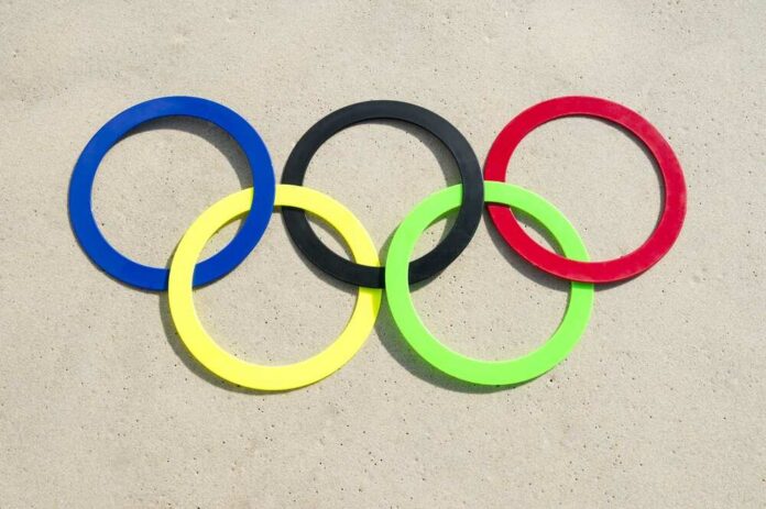 Colorful Olympic rings arranged on sandy surface