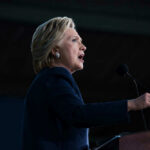 Clinton GRILLED on Epstein — Her Answer STUNS Hillary Clinton speaking at podium with a microphone.