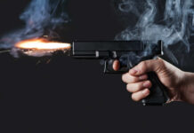 A hand holding a gun with smoke and a flash from the muzzle