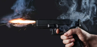 A hand holding a gun with smoke and a flash from the muzzle