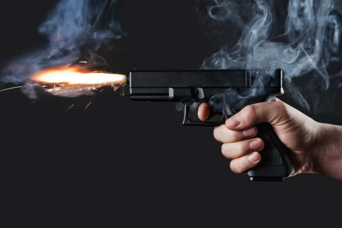A hand holding a gun with smoke and a flash from the muzzle