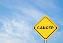 Yellow warning sign displaying the word 'CANCER' against a blue sky