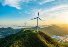 Wind turbines on a green hillside during sunset