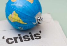 A small globe resting on a newspaper with the word 'crisis'