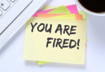 A sticky note with the message 'YOU ARE FIRED' placed on a desk next to a keyboard and a cup of coffee